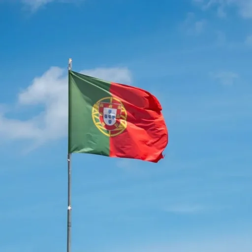 Bandeira de Portugal a ondear num mastro sob um céu azul com nuvens, simbolizando o lançamento do portal Portugal EuroBrief.